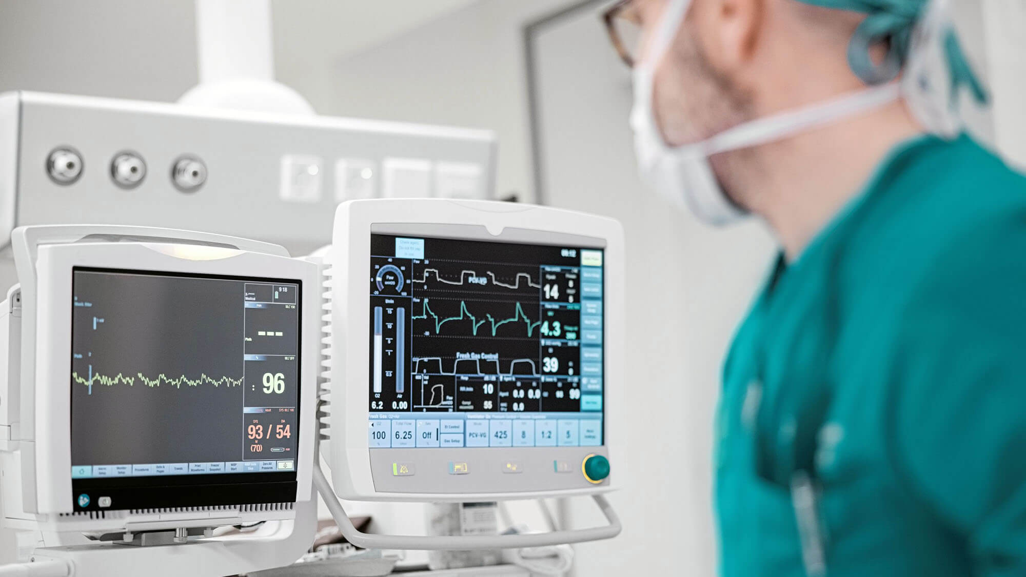Male surgeon looking at the monitoring equipment during surgery. Doctor in medical scrubs performing operation in operating room and looking at pulse trace on monitors.
